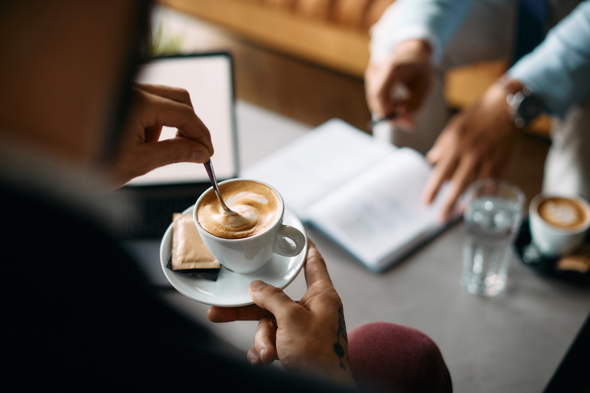 Close up of businessman drinking coffee during meeting with colleague in a cafe.