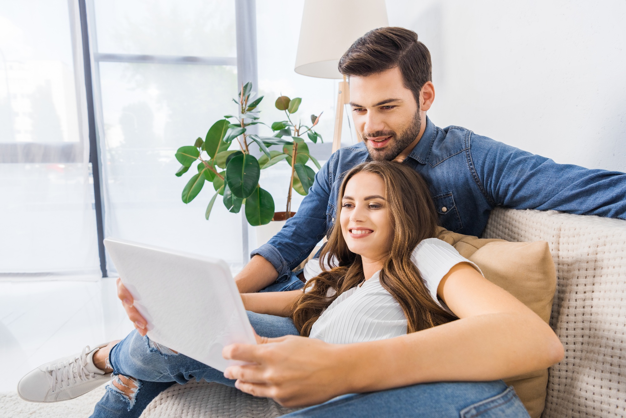 smiling young couple sitting on couch and watching digital tablet at home